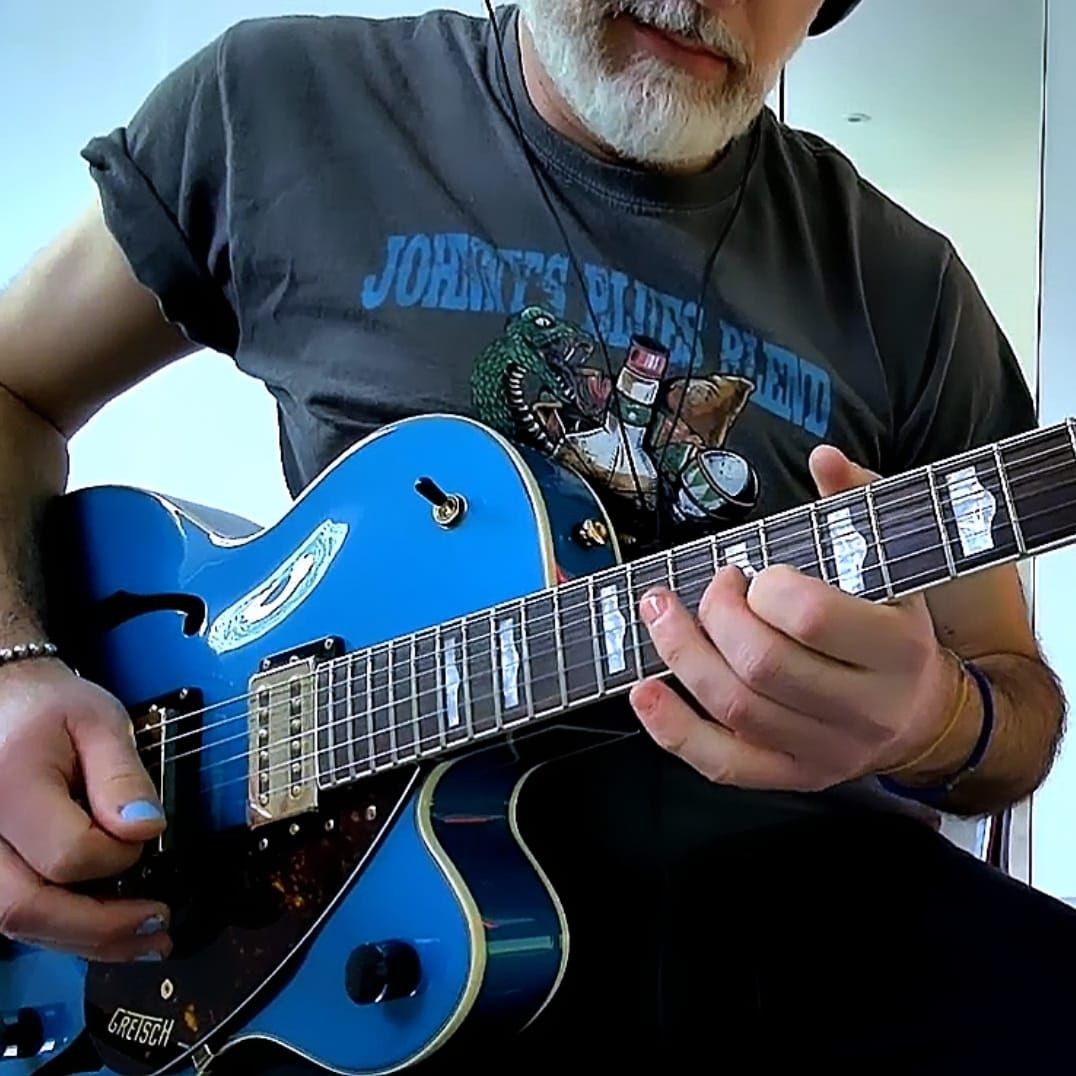 Man playing a blue electric guitar while wearing headphones and a T-shirt with graphics.