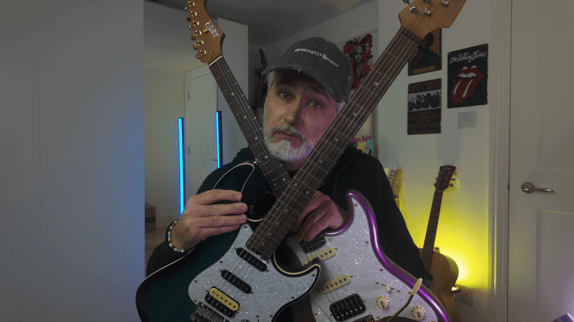 Person holding two electric guitars in a music-themed room with posters on the wall.