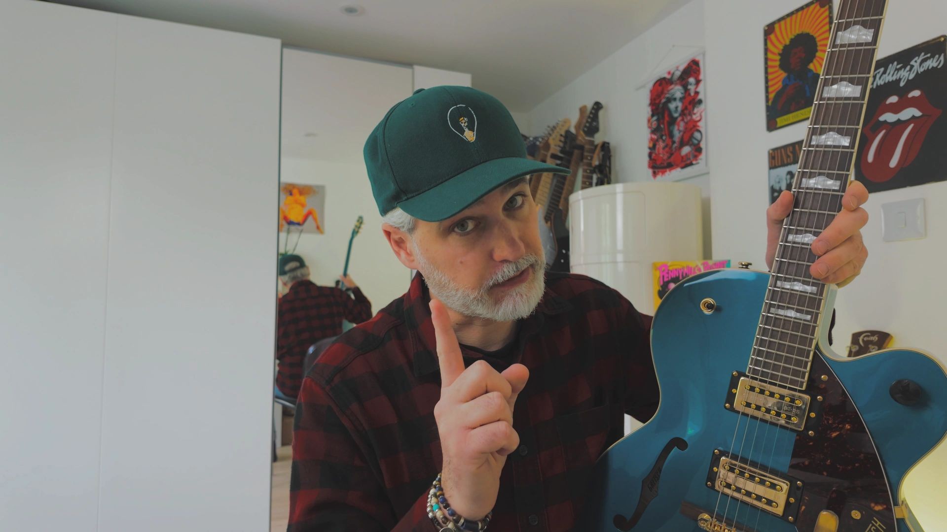 Person holding a blue electric guitar in a room decorated with various posters and musical equipment.